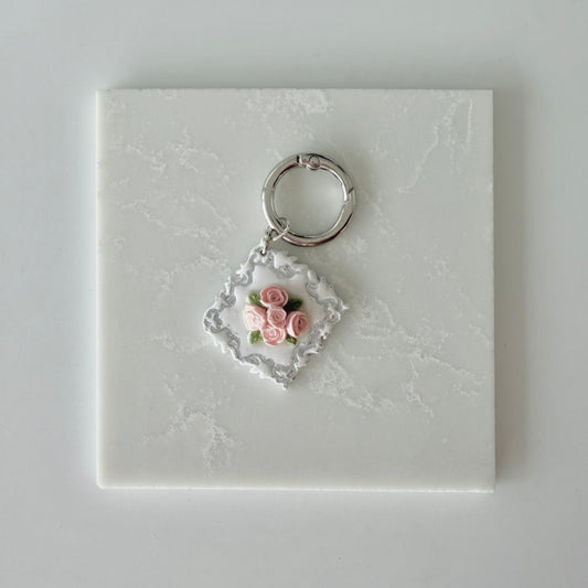 Large Diamond shape pet id tag with 5 pink roses, 4 green leaves, and silver engraving on a white marble background.