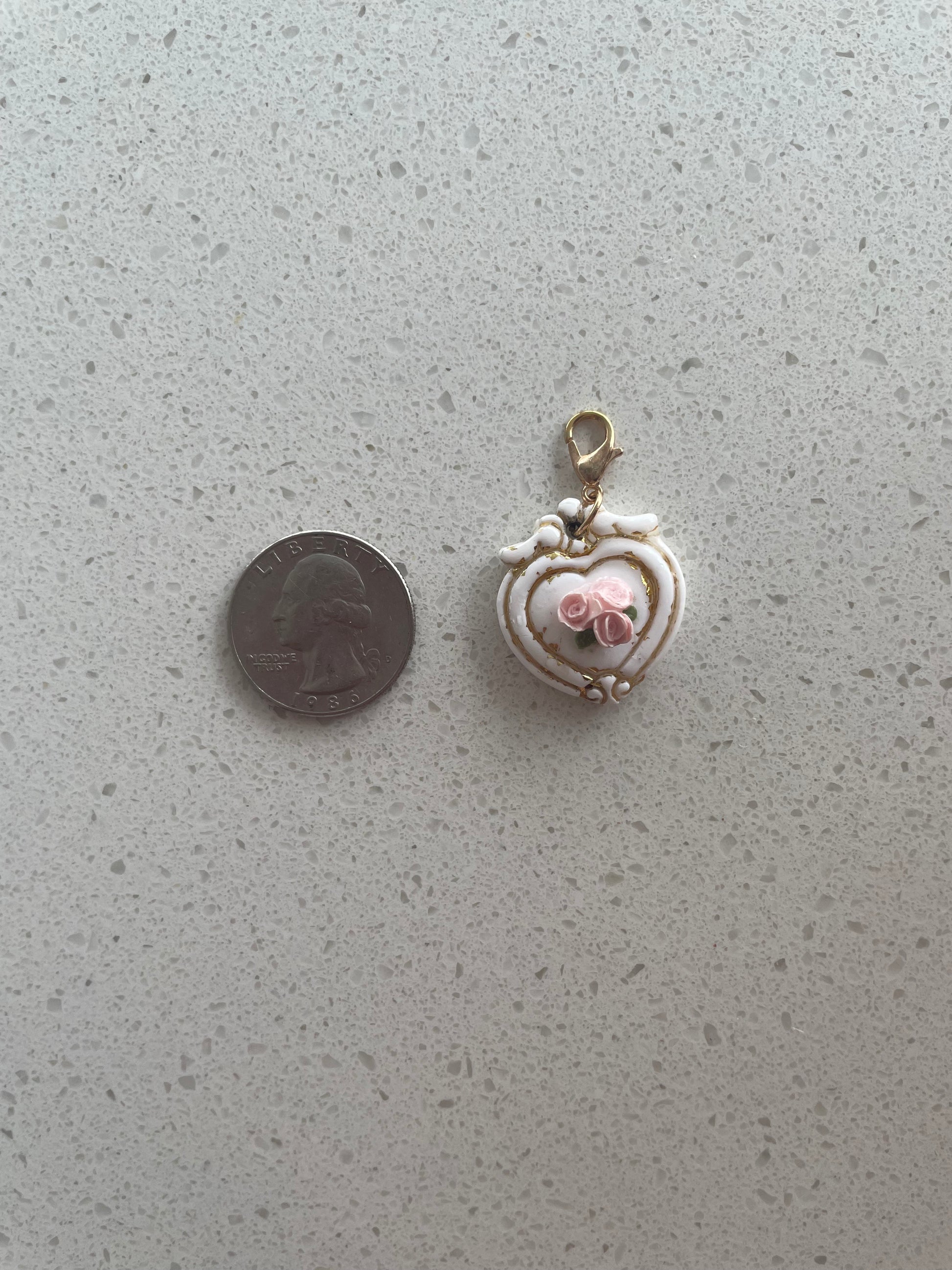 Small decorative heart-shaped object on a textured gray surface with a coin for scale.