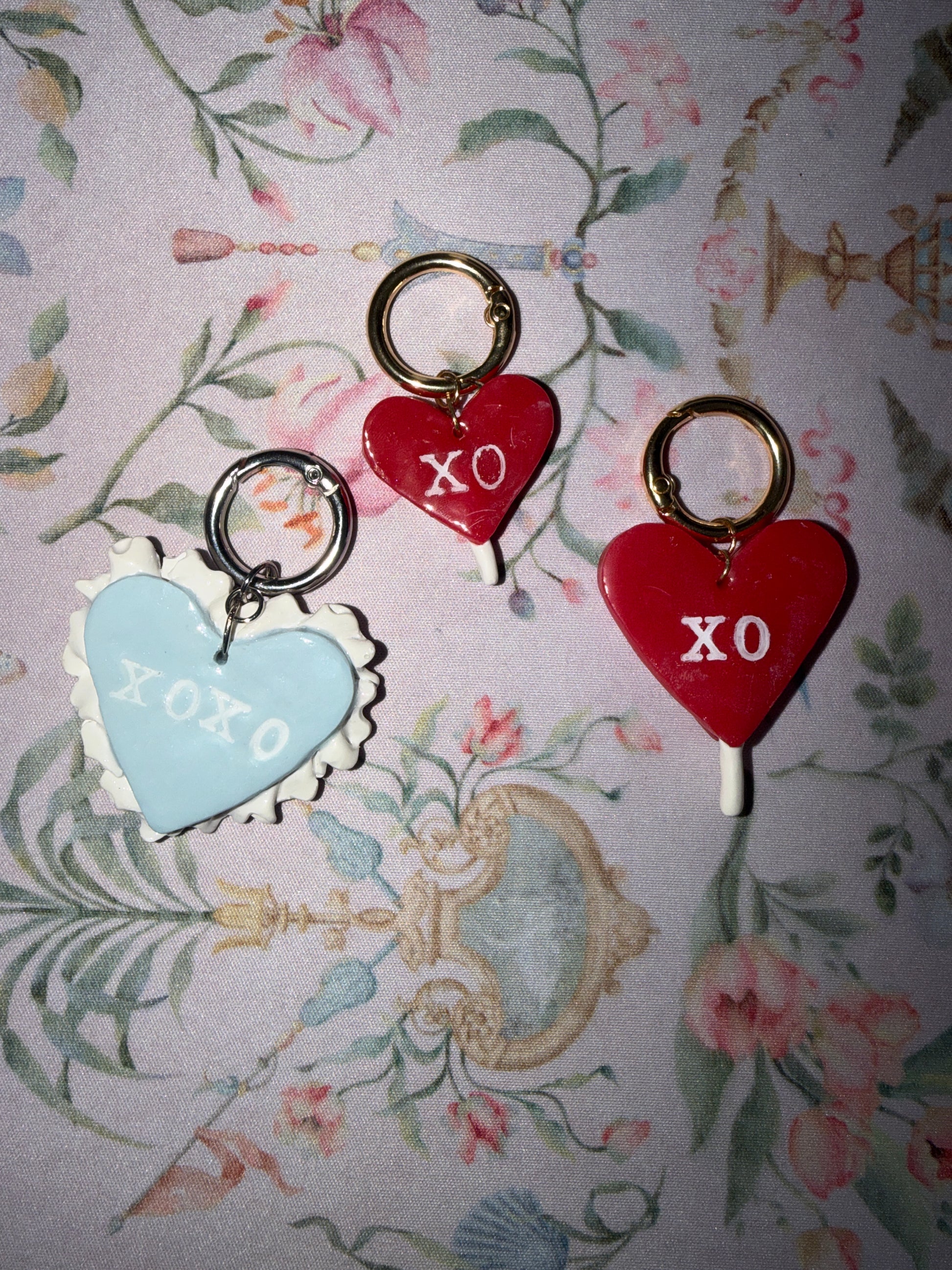 Heart-shaped valentines lollypop charms with 'XO' text on a floral-patterned background