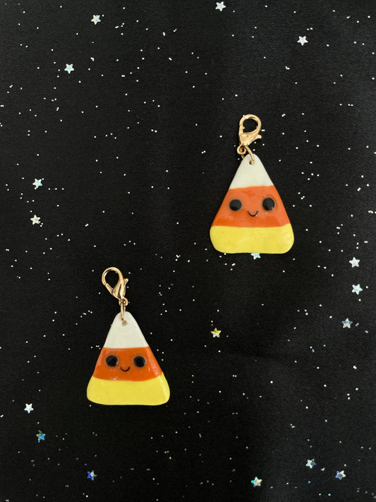 Two candy corn-shaped charms on a black background with star patterns