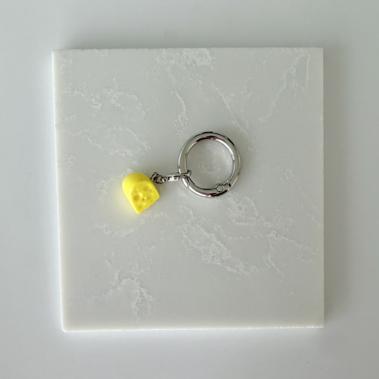 Yellow cheese slice with holes and lobster clasp attached to larger o ring 