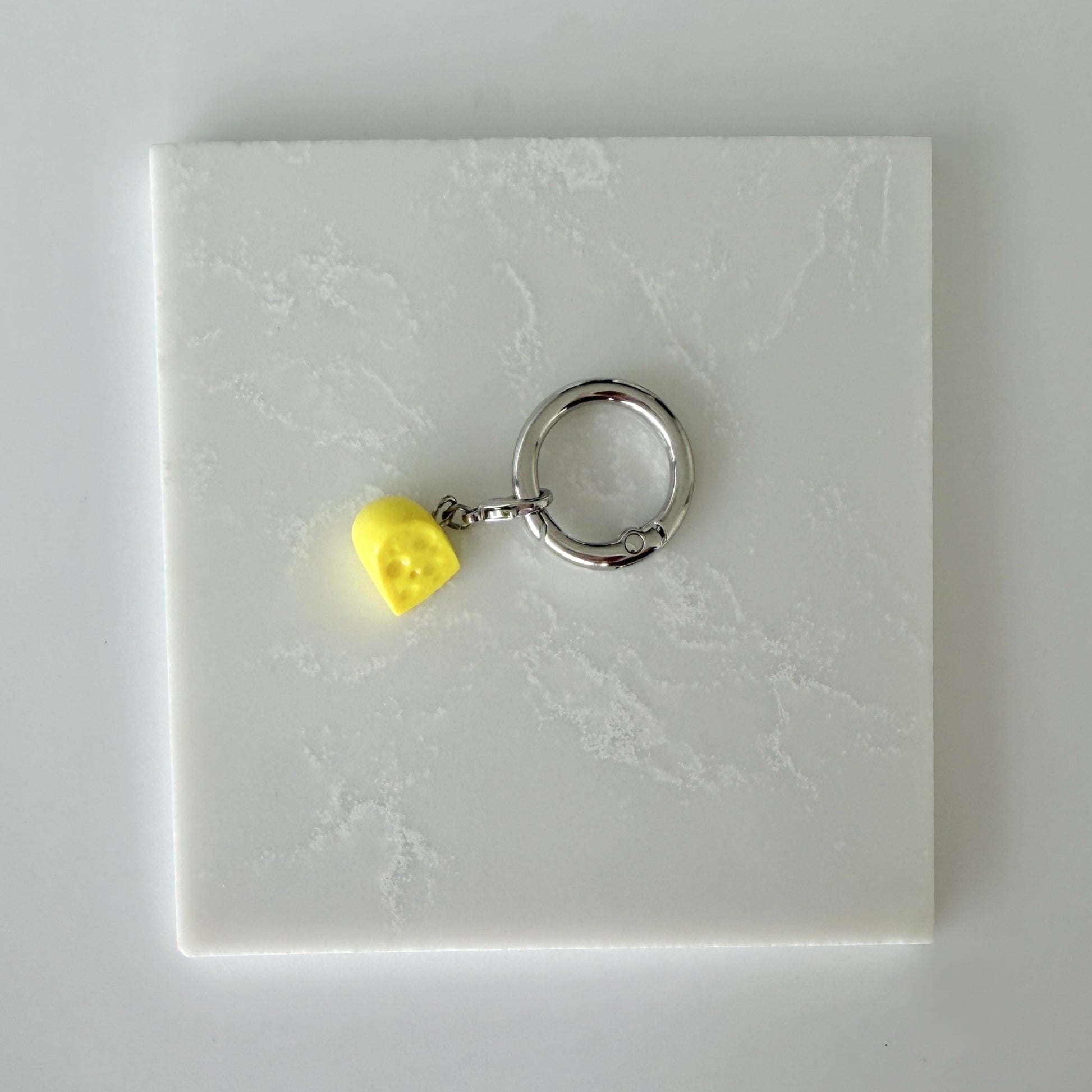 Yellow cheese slice with holes and lobster clasp attached to larger o ring 