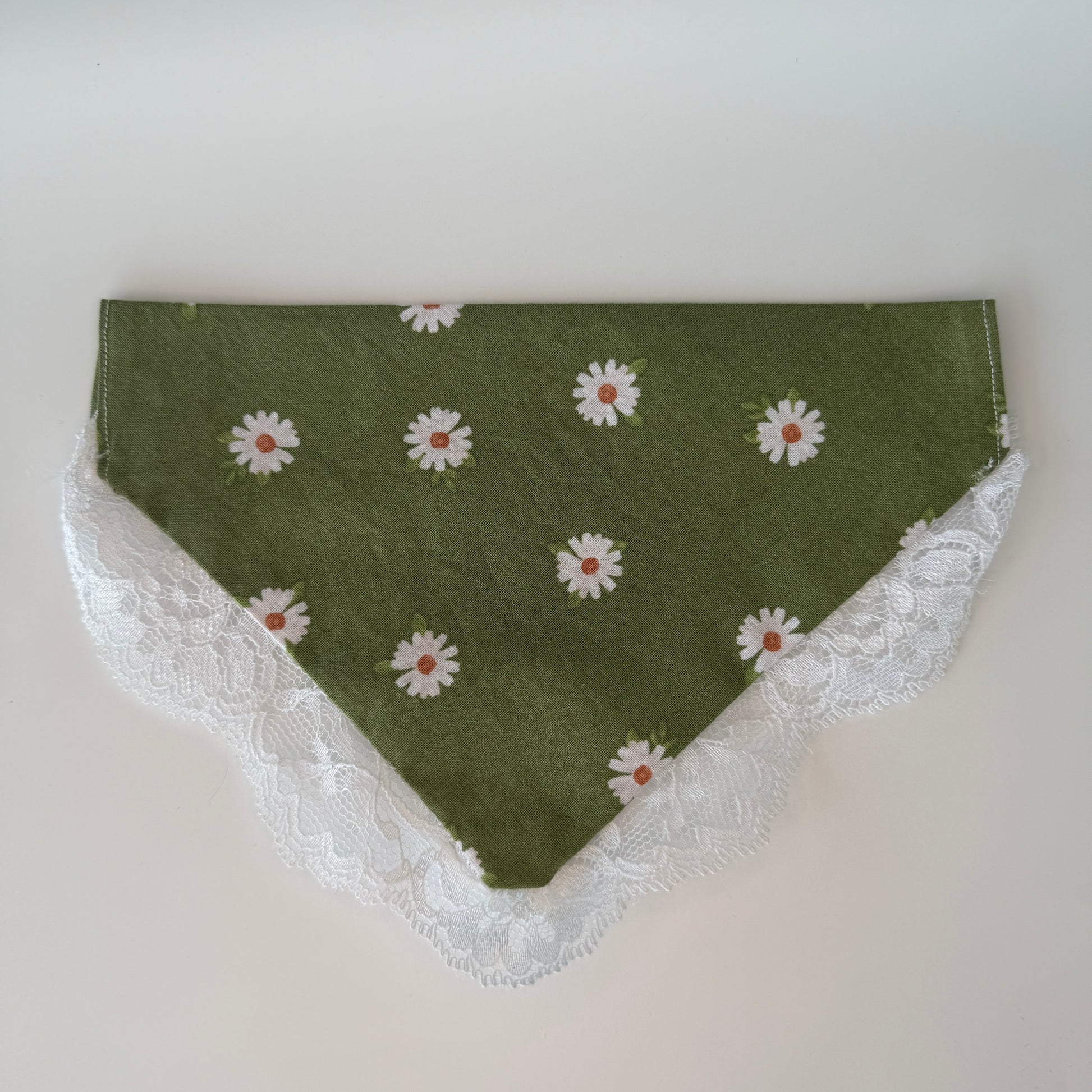 Green dog bandana with white daisy pattern and lace trim on a light gray background