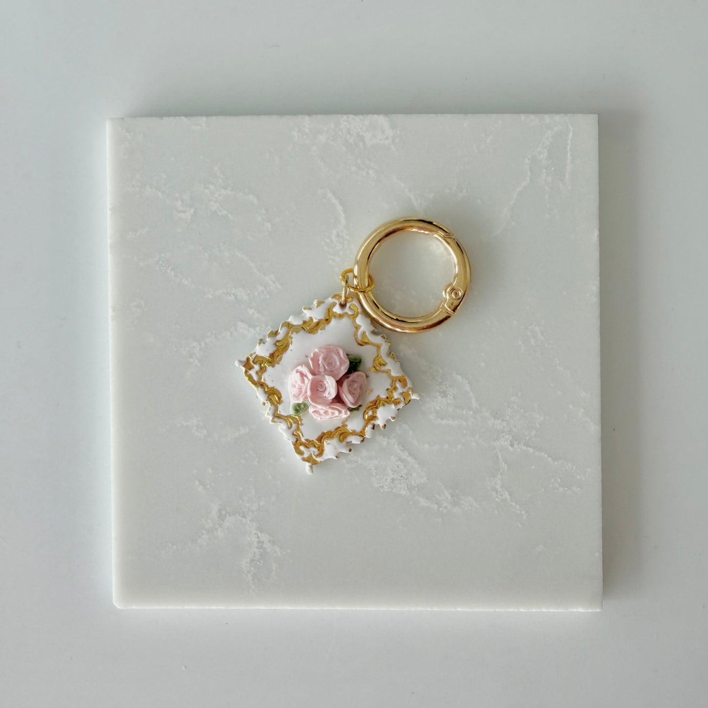 Large Diamond shape pet id tag with 5 pink roses, 4 green leaves, and gold engraving on a white marble background.