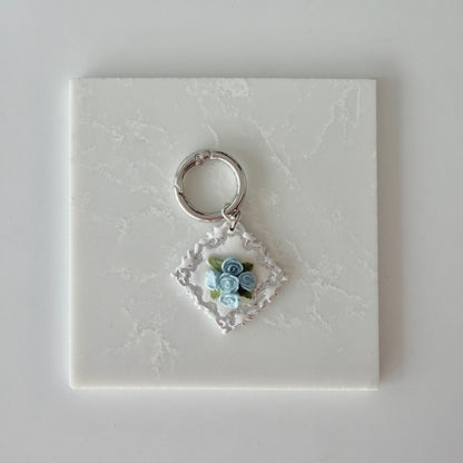 Large Diamond shape pet id tag with 5 blue roses, 4 green leaves, and silver engraving on a white marble background.