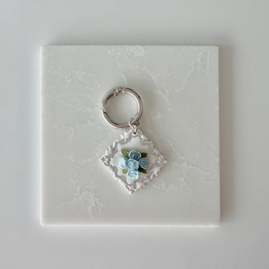 Large Diamond shape pet id tag with 5 blue roses, 4 green leaves, and silver engraving on a white marble background.
