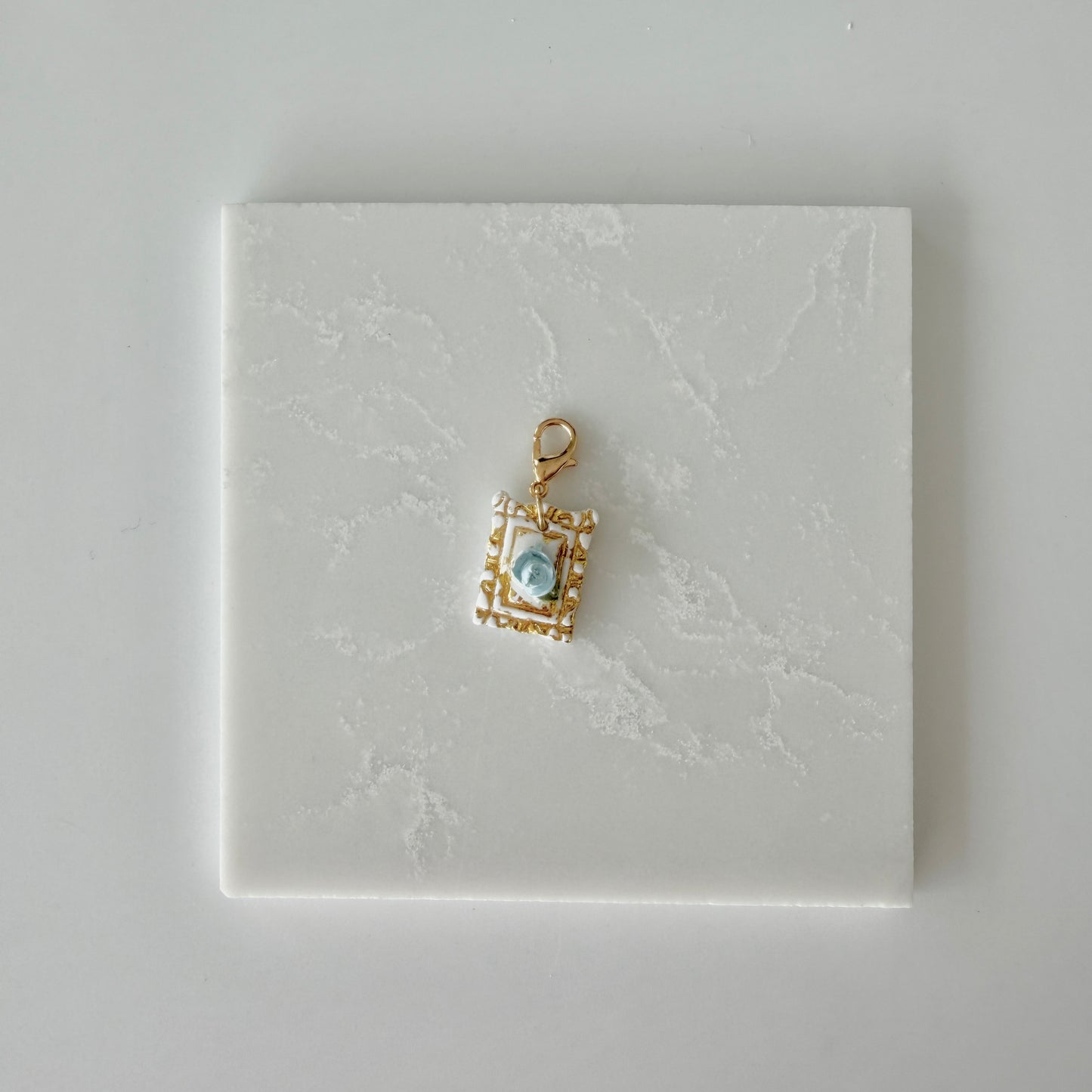 Small pet tag with gold engraving and single blue rose on a white marble background