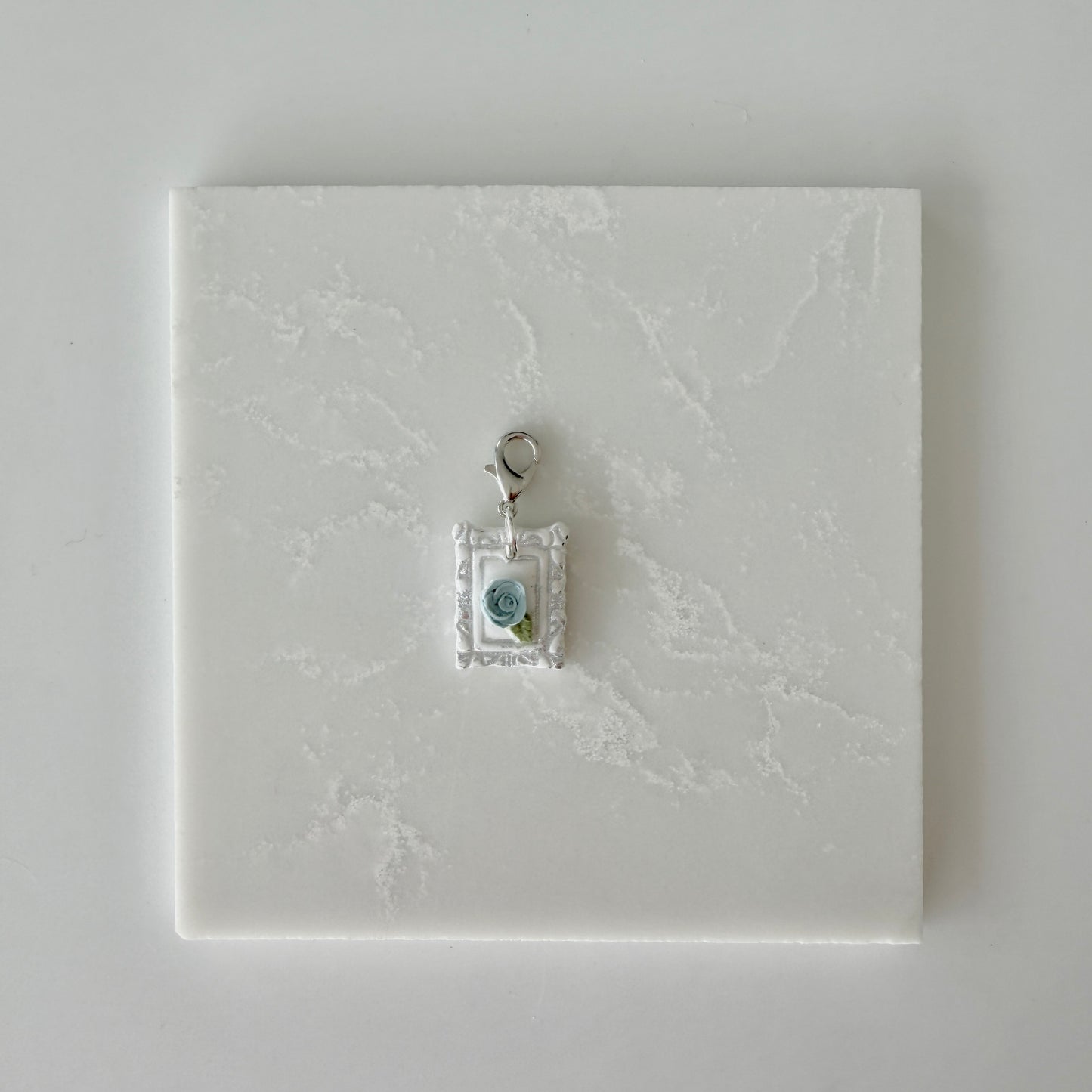 Small pet tag with silver engraving and single blue rose on a white marble background