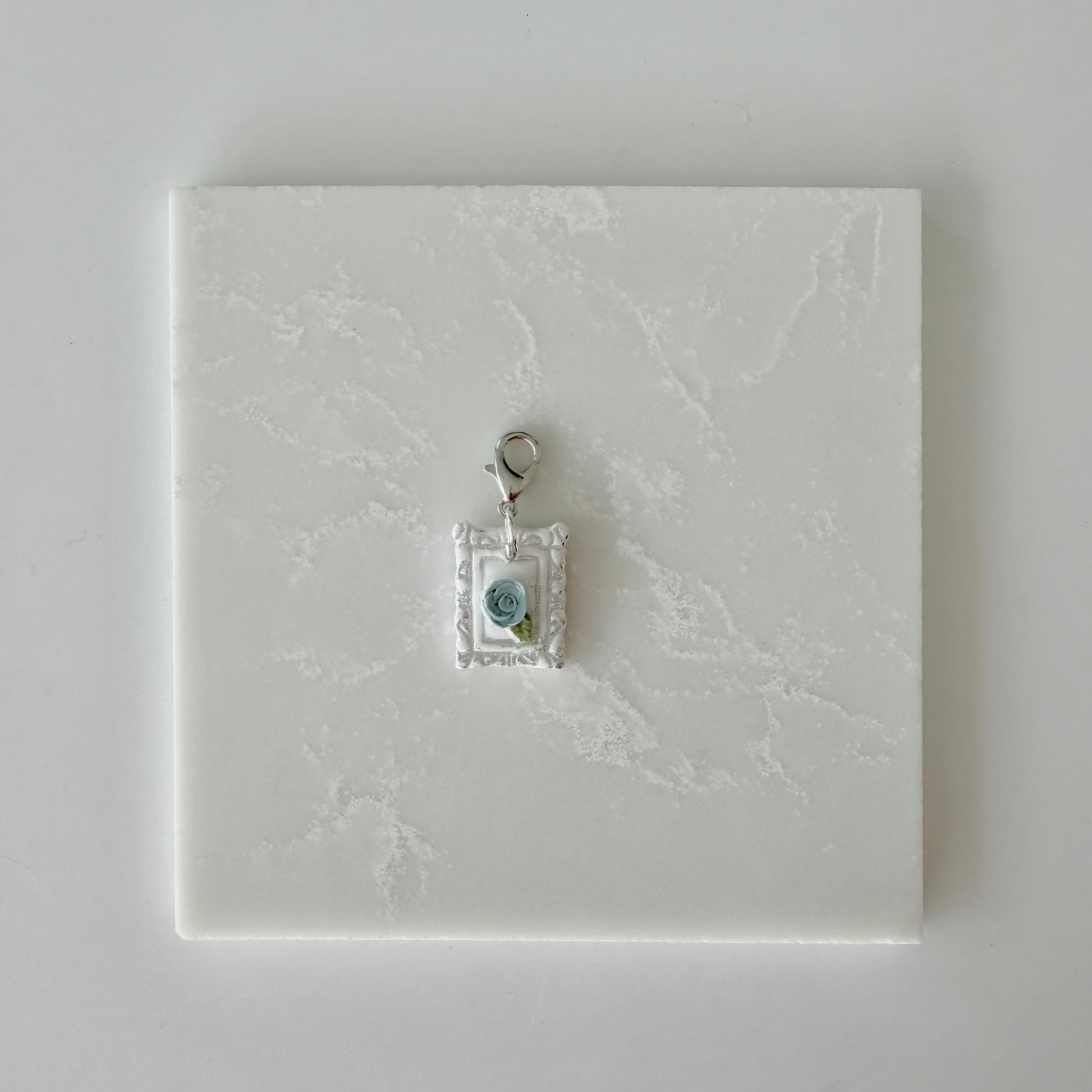 Small pet tag with silver engraving and single blue rose on a white marble background