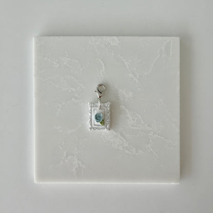 Small pet tag with silver engraving and single blue rose on a white marble background