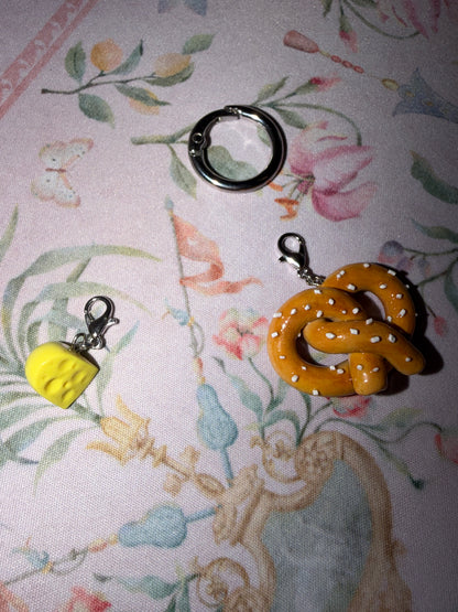 Cheese tax charm and soft pretzel charm laying next to each other on a floral background
