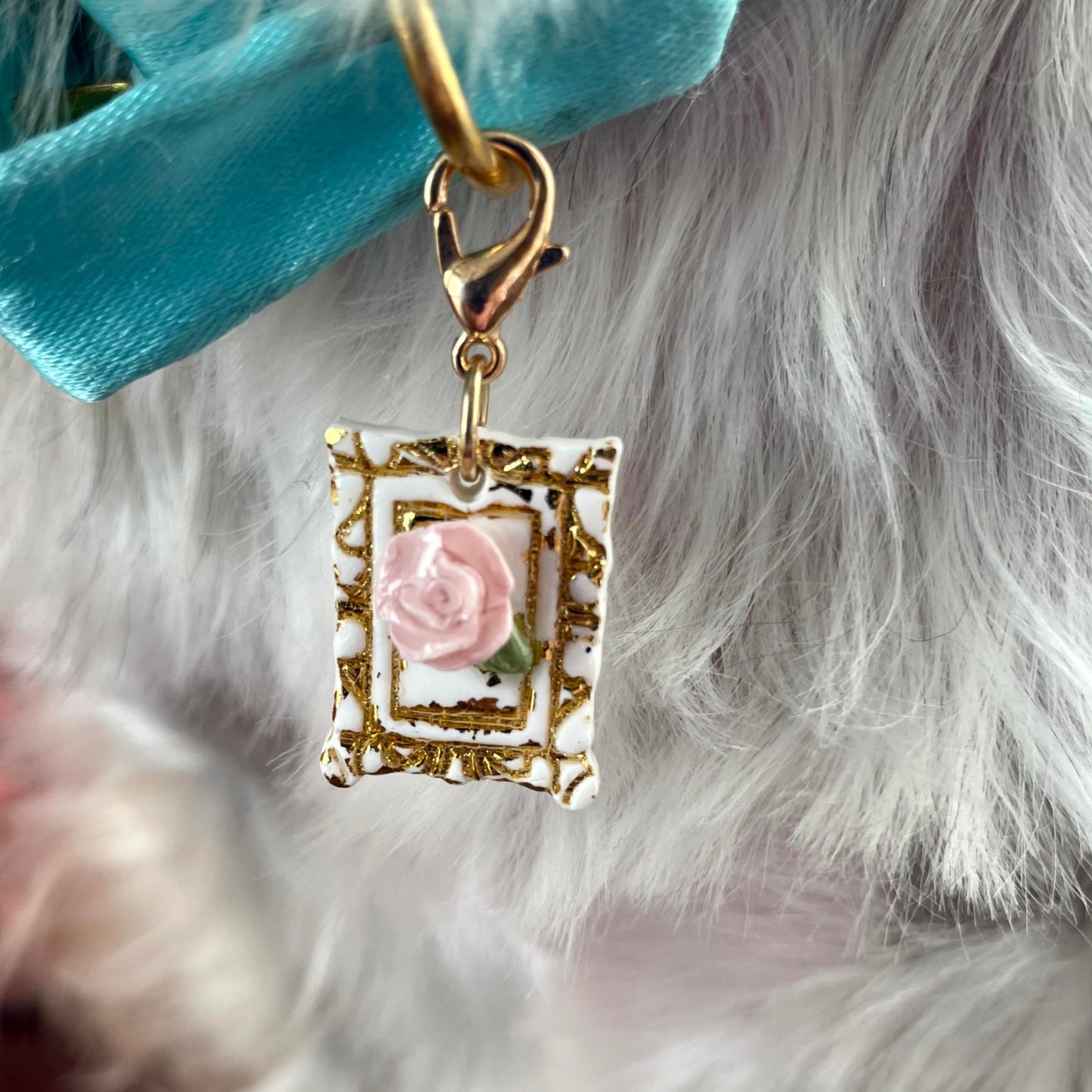 Close-up of a decorative dog tag with a pink rose design hanging from the collar of a grey and white dog