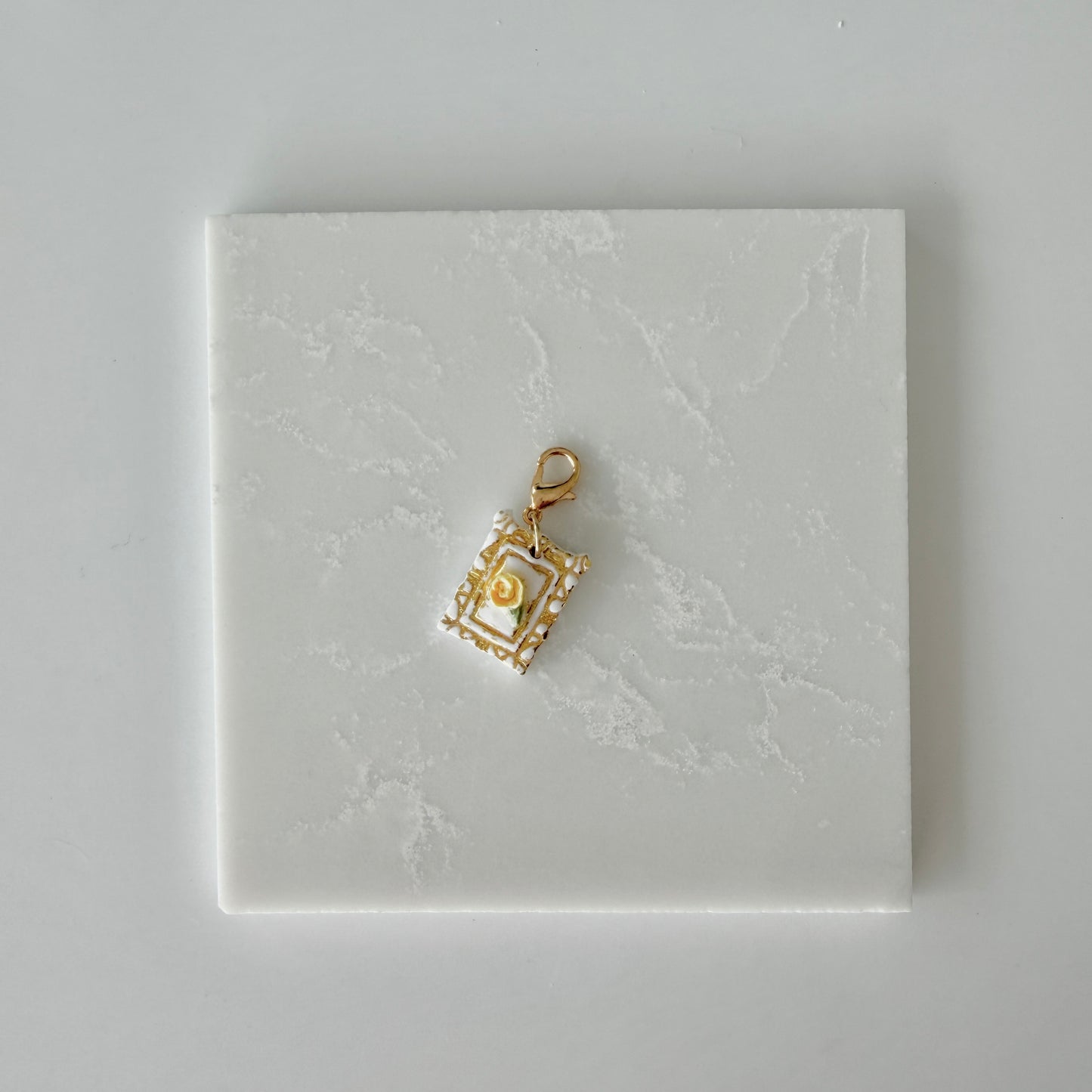 Small pet tag with gold engraving and single yellow rose on a white marble background