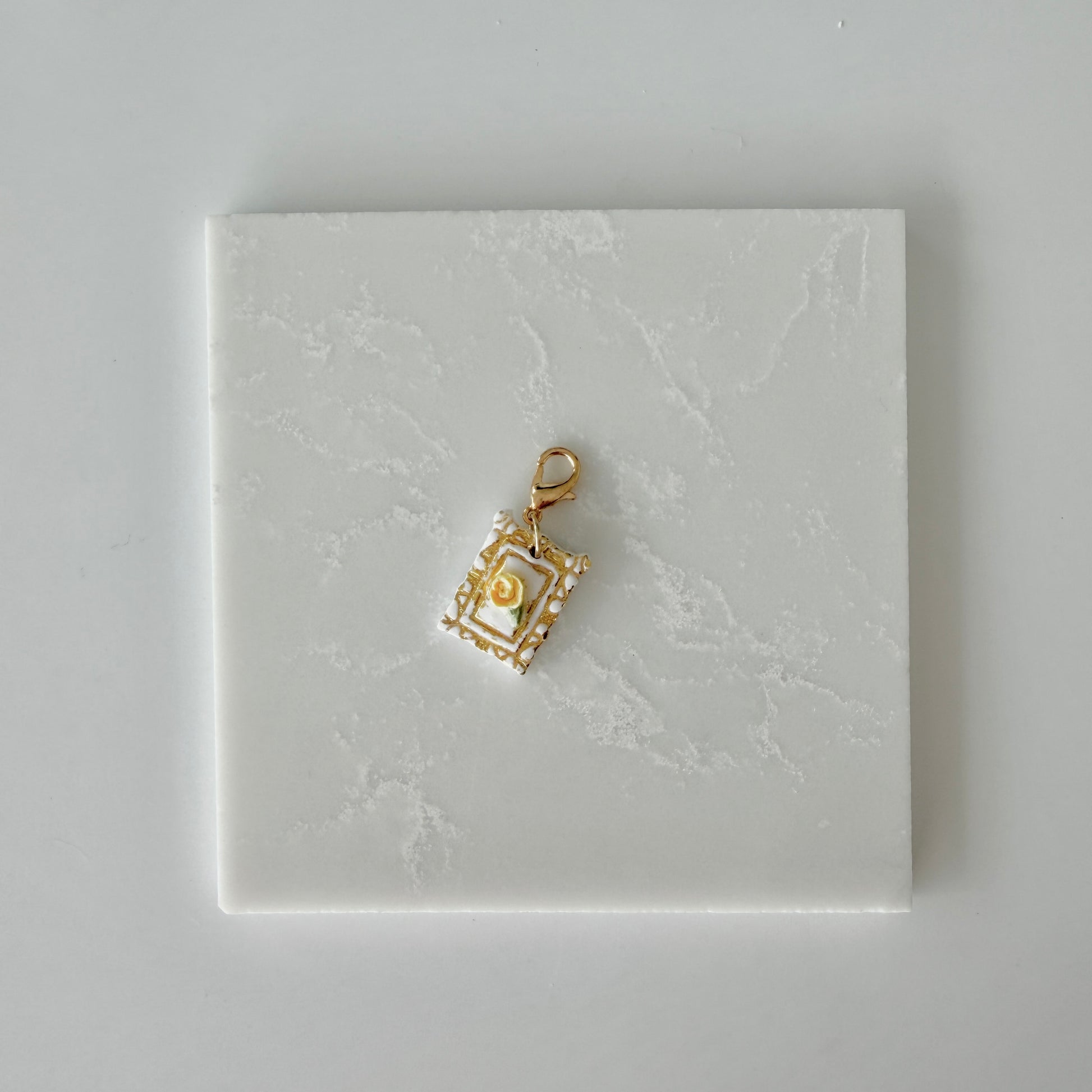 Small pet tag with gold engraving and single yellow rose on a white marble background