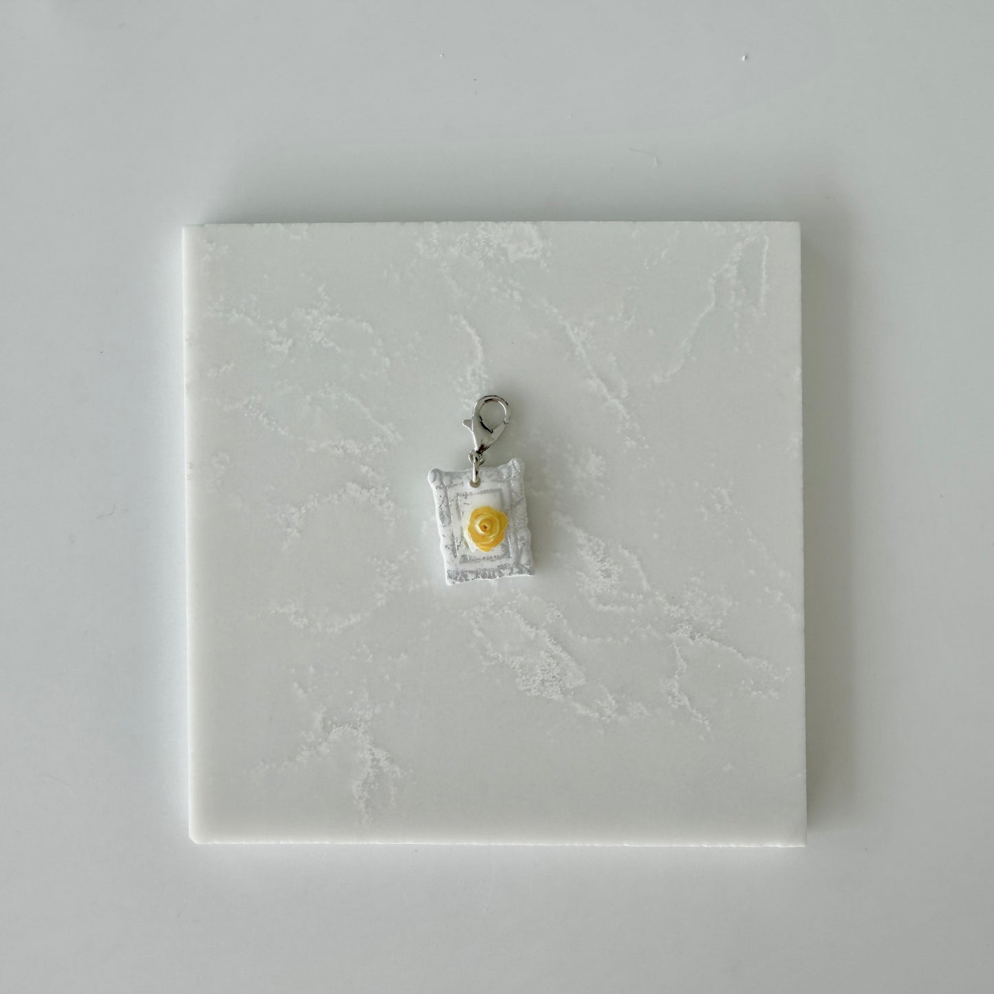 Small pet tag with silver engraving and single yellow rose on a white marble background