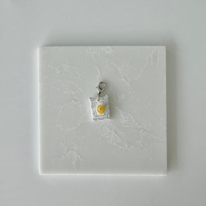 Small pet tag with silver engraving and single yellow rose on a white marble background