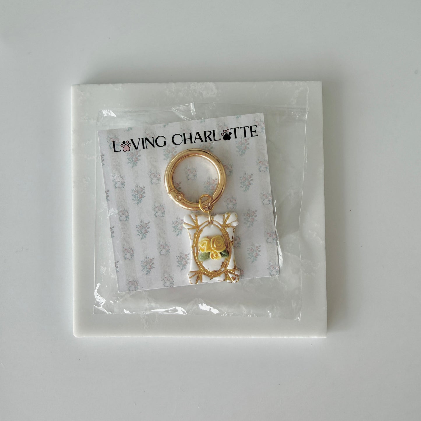 Rectangle pet id tag with 3 yellow roses and gold gilding on a 'Loving Charlotte' branded card in clear packaging.