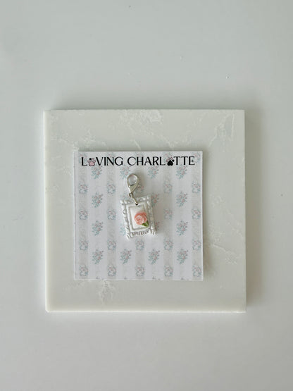 Small pet tag with silver engraving and single pink rose on a card with 'Loving Charlotte' branding on a light gray background