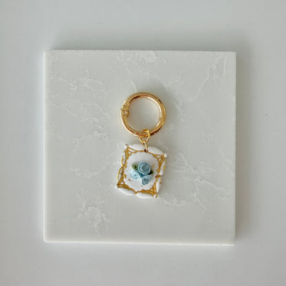 Dog tag with blue and gold floral design on a white marble surface