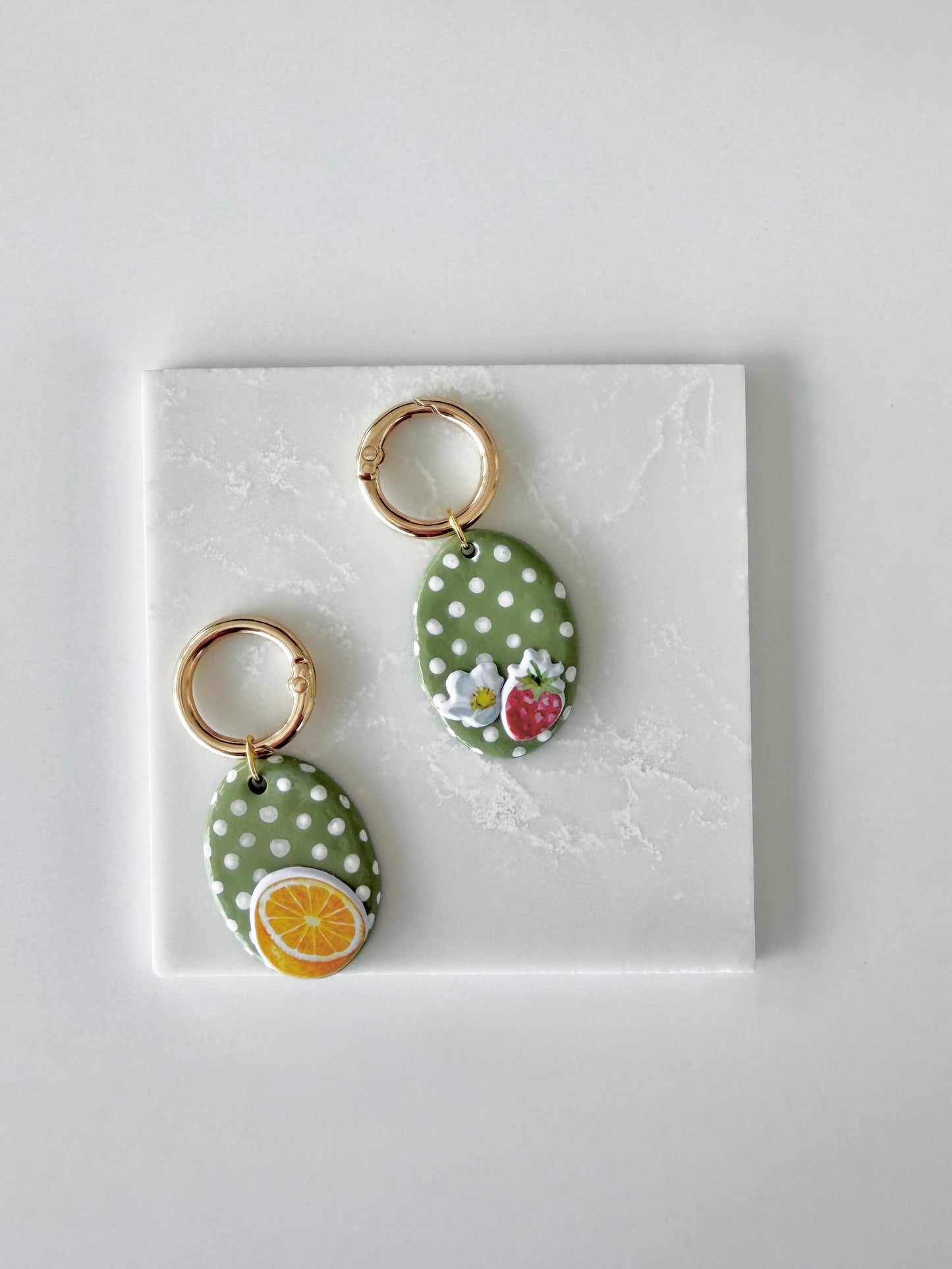 Two oval shaped pet tags with gold hardware sitting side by side one has an range slice design then other a strawberry and flower. This is a blank product image you can customize